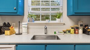 A kitchen with a stainless steel sink, blue cabinets, and a window with blinds. - Book Coastal Cottage – Short Drive to the Beach! (Gulf Shores)