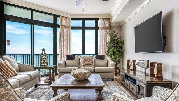 A spacious living room with a large window, a flat-screen TV, and a comfortable seating area. - The Oasis at Orange Beach #1707 (Orange Beach)