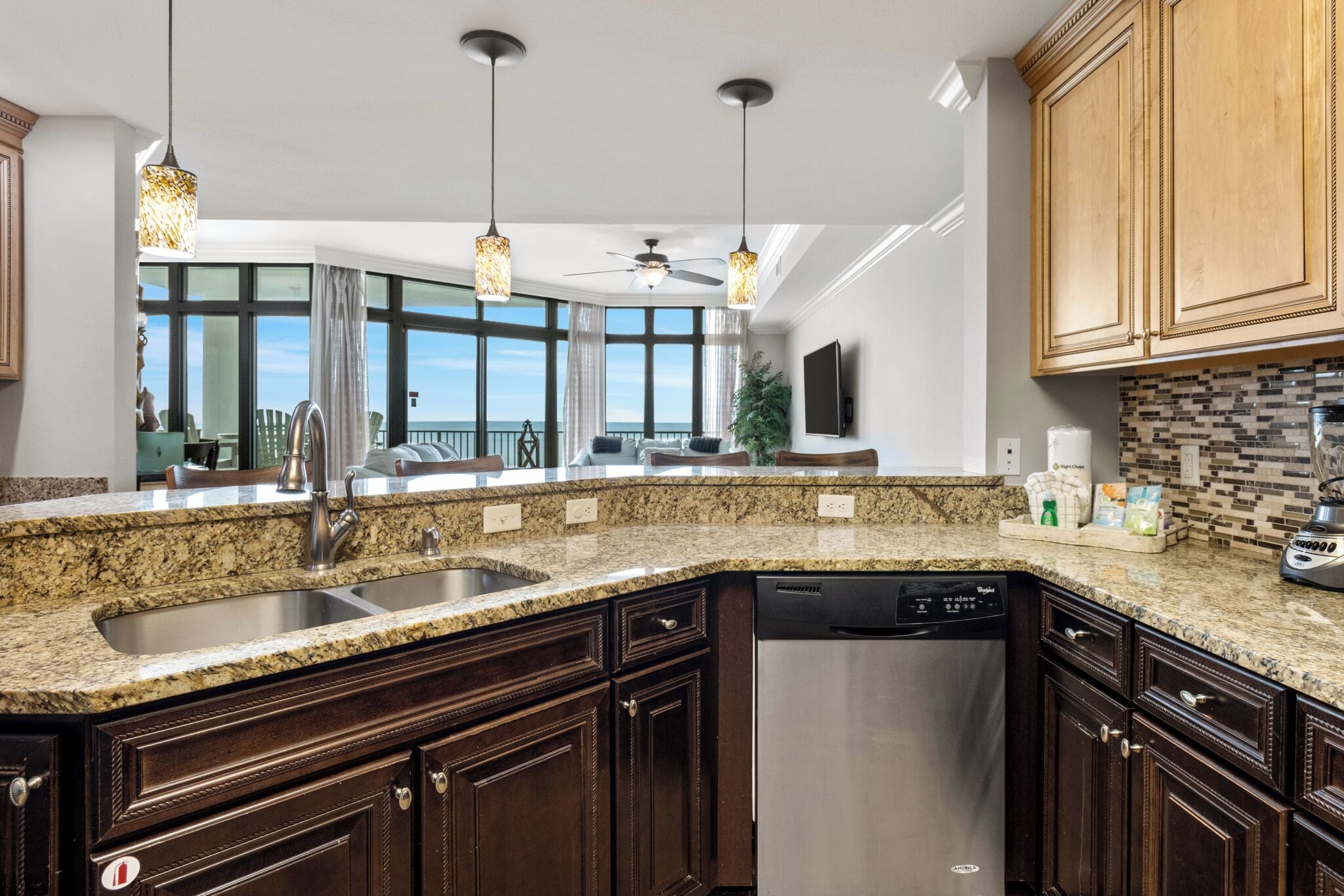 A kitchen with granite countertops, dark wood cabinets, stainless steel appliances, and pendant lighting.