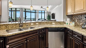 A kitchen with granite countertops, dark wood cabinets, stainless steel appliances, and pendant lighting. - The Oasis at Orange Beach #1707 (Orange Beach)