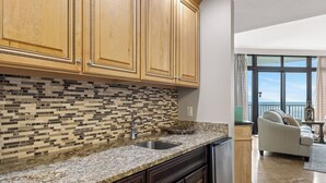 A kitchen with wooden cabinets, a tiled backsplash, granite countertops, and a built-in sink. - The Oasis at Orange Beach #1707 (Orange Beach)