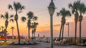 A poolside area with lounge chairs and palm trees, overlooking a beach at sunset. - The Oasis at Orange Beach #1707 (Orange Beach)