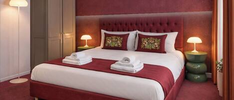 Une chambre d’hôtel avec un grand lit, deux tables de chevet avec des lampes, une armoire et un sol recouvert d’une moquette rouge.