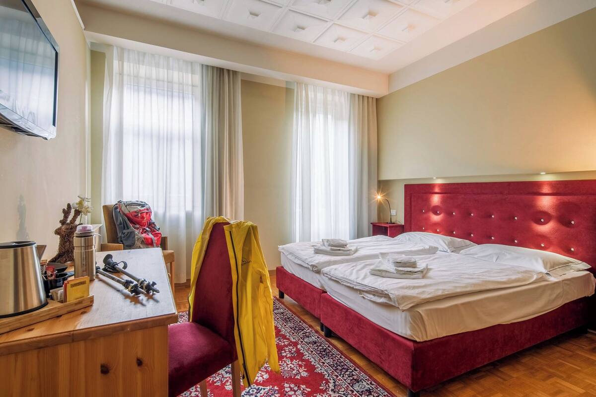 Ein Hotelzimmer mit Bett, Schreibtisch mit Stuhl, Fernseher und einem fensterbepflanzten Fenster.
