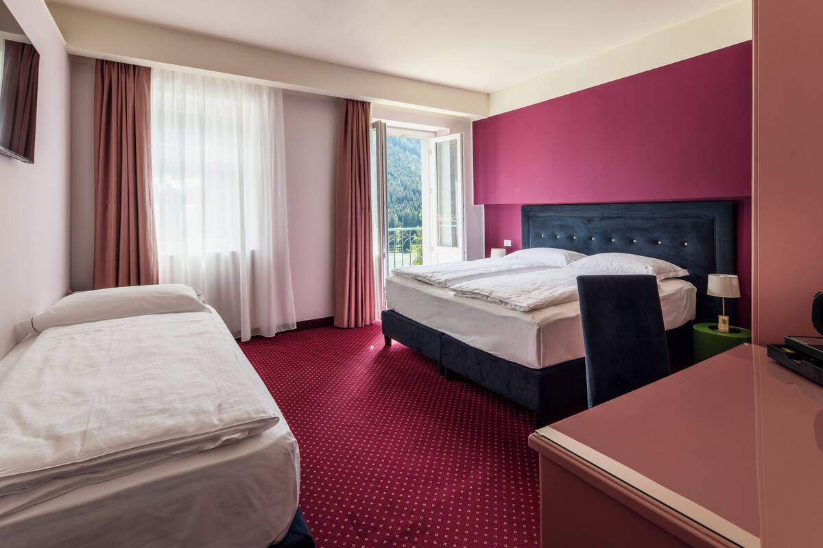 Ein Hotelzimmer mit Bett, Schreibtisch, Stuhl, Nachttisch und einem Fenster mit Vorhängen.