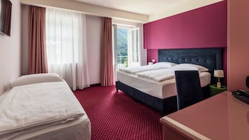 Une chambre d’hôtel avec un lit, un bureau, une chaise, une table de chevet et une fenêtre avec des rideaux.