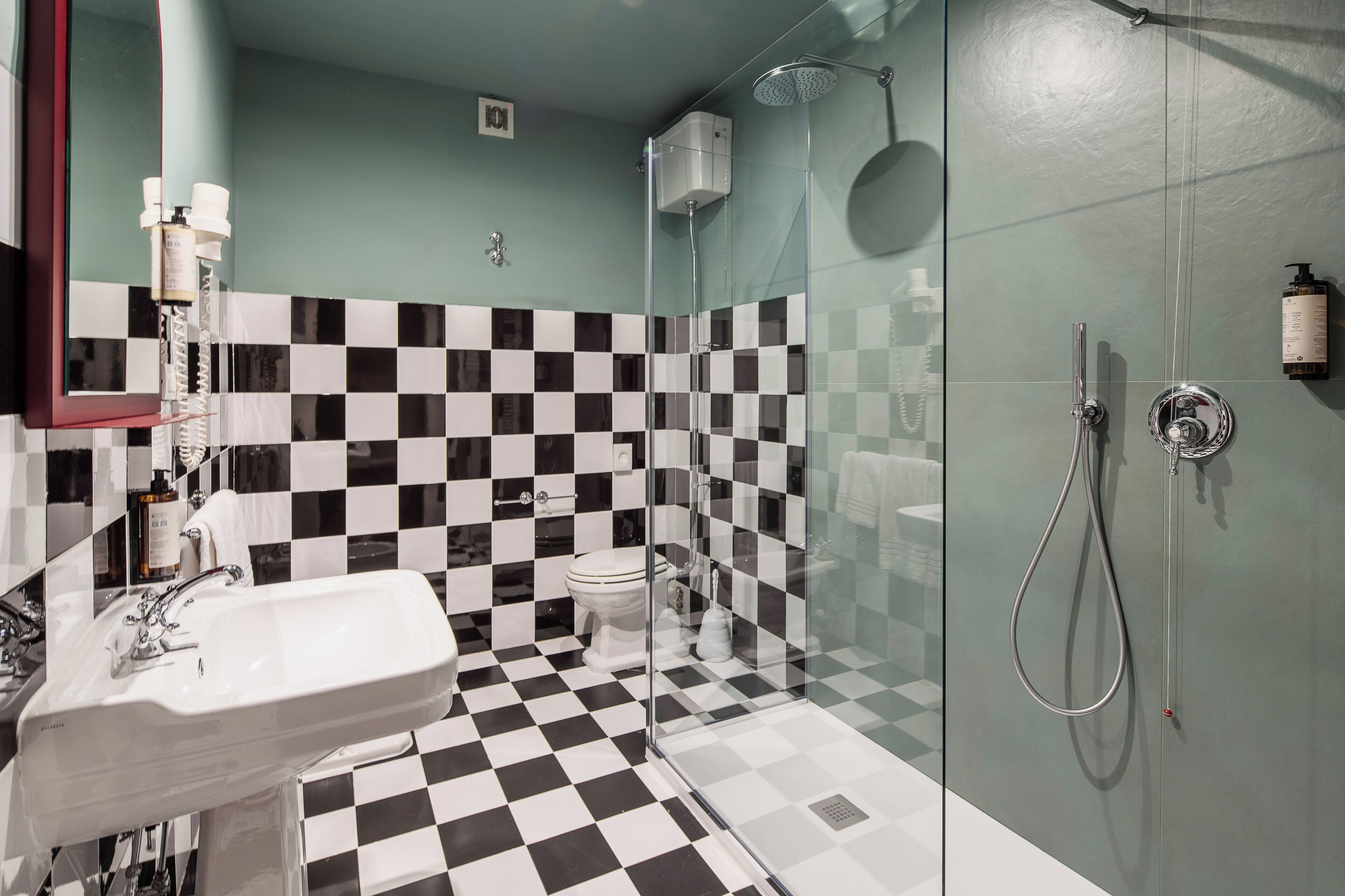 Un baño con piso a cuadros, cabina de ducha de vidrio, lavamanos y retrete.