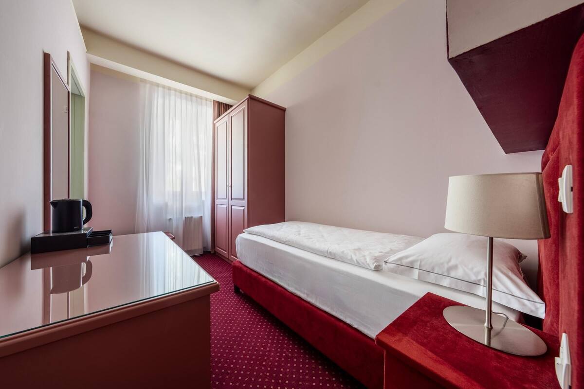 Ein Hotelzimmer mit einem Bett, einem Schreibtisch, einem Stuhl, einer Lampe und einem Kleiderschrank.