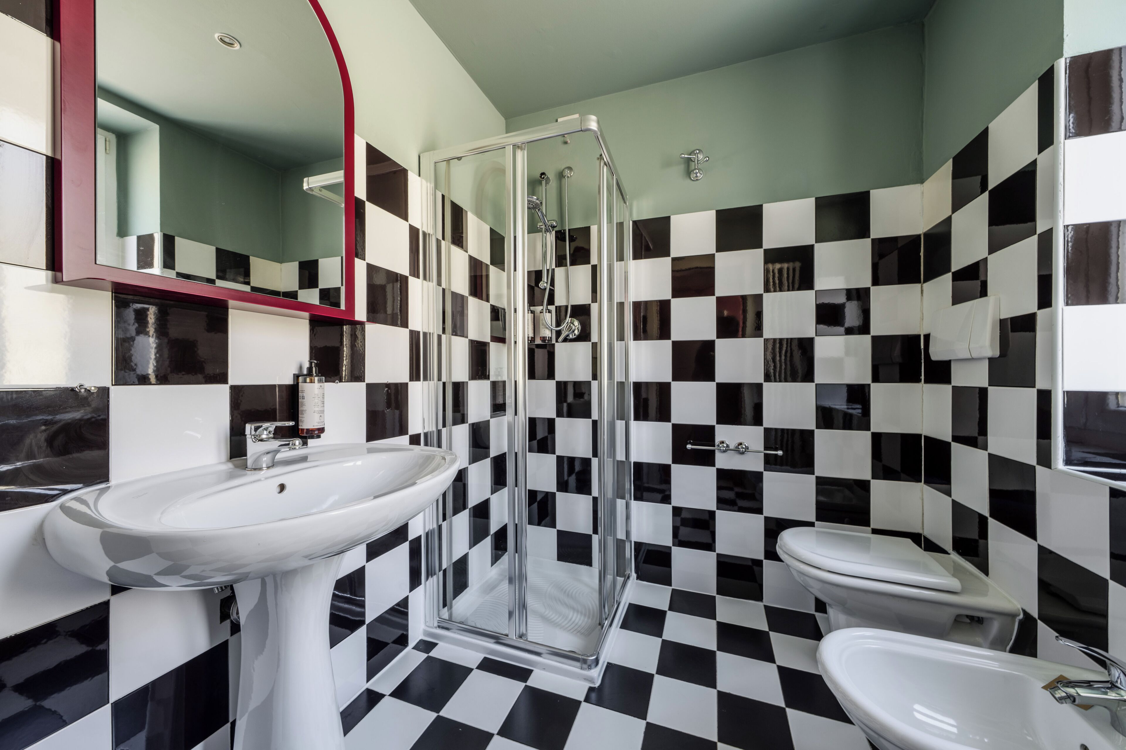 A bathroom with a checkered floor, a glass shower enclosure, and a white sink.