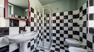 Un baño con piso a cuadros, cabina de ducha de vidrio y lavamanos blanco.