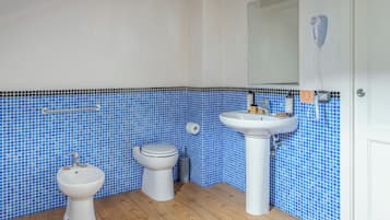 Un baño con inodoro, bidé y lavamanos, todos con accesorios blancos. Las paredes están revestidas con mosaicos azules.