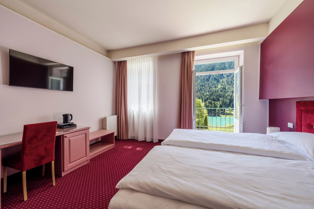 A hotel room with a bed, desk, chair, and a TV.