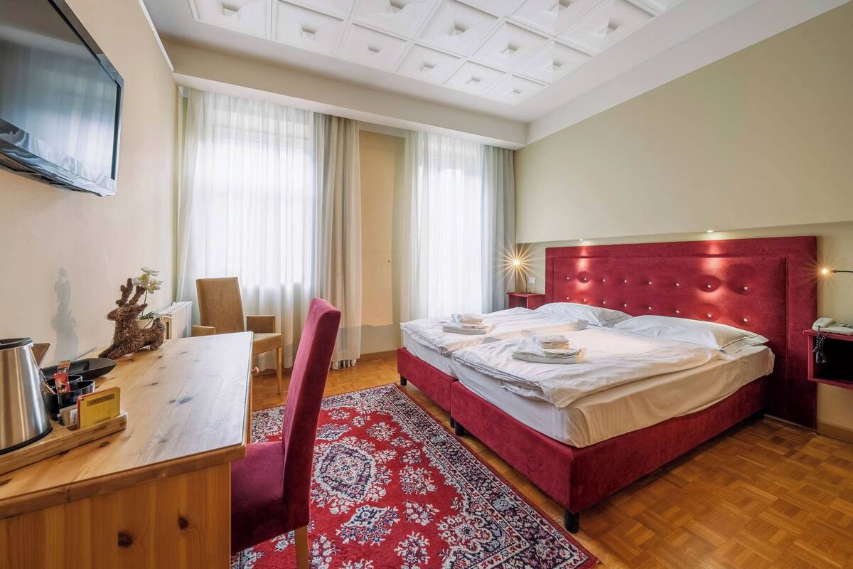 Ein Hotelzimmer mit Bett, Schreibtisch, Stuhl, Fernseher und einem Fenster mit Vorhängen.