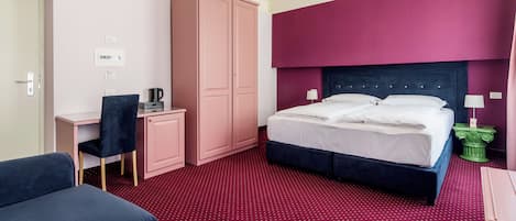Una habitación de hotel con cama, escritorio, silla, armario y alfombra roja.