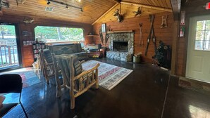 Interior acogedor de una cabaña con chimenea de piedra, muebles de madera y un ventilador de techo.