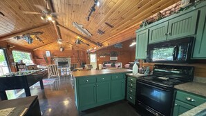 Una cocina amplia con gabinetes verdes, una estufa negra y un comedor con mesa de fútbol.