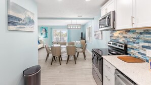 A modern kitchen with a central island, a dining area with a glass table, and a view of the outdoors. - Blue Dolphin (Santa Rosa Beach)