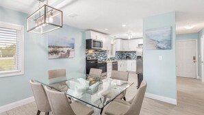 A modern kitchen with white cabinets, a glass dining table, and beige chairs. - Blue Dolphin (Santa Rosa Beach)