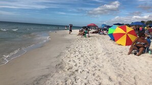 A beach with people relaxing under colorful umbrellas, a sandy shore, and the ocean in the background. - Gated Community, SALT pool, Miles of Walking Paths, Tropical Paradise-Near Beach (Naples)