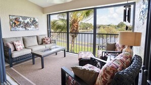 A spacious living area with a sofa, coffee table, and a view of a lake through large sliding glass doors.