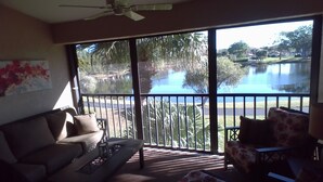 A living room with a large window overlooking a lake, a ceiling fan, and a couch.