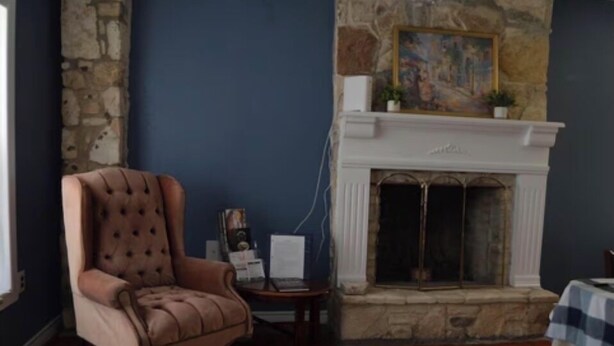 Une pièce avec une cheminée en pierre, un fauteuil à capitons, une petite table avec un ordinateur portable et un tableau au-dessus de la cheminée.