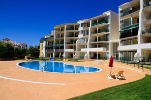 Un hotel moderno con piscina, varios balcones y un césped bien cuidado.