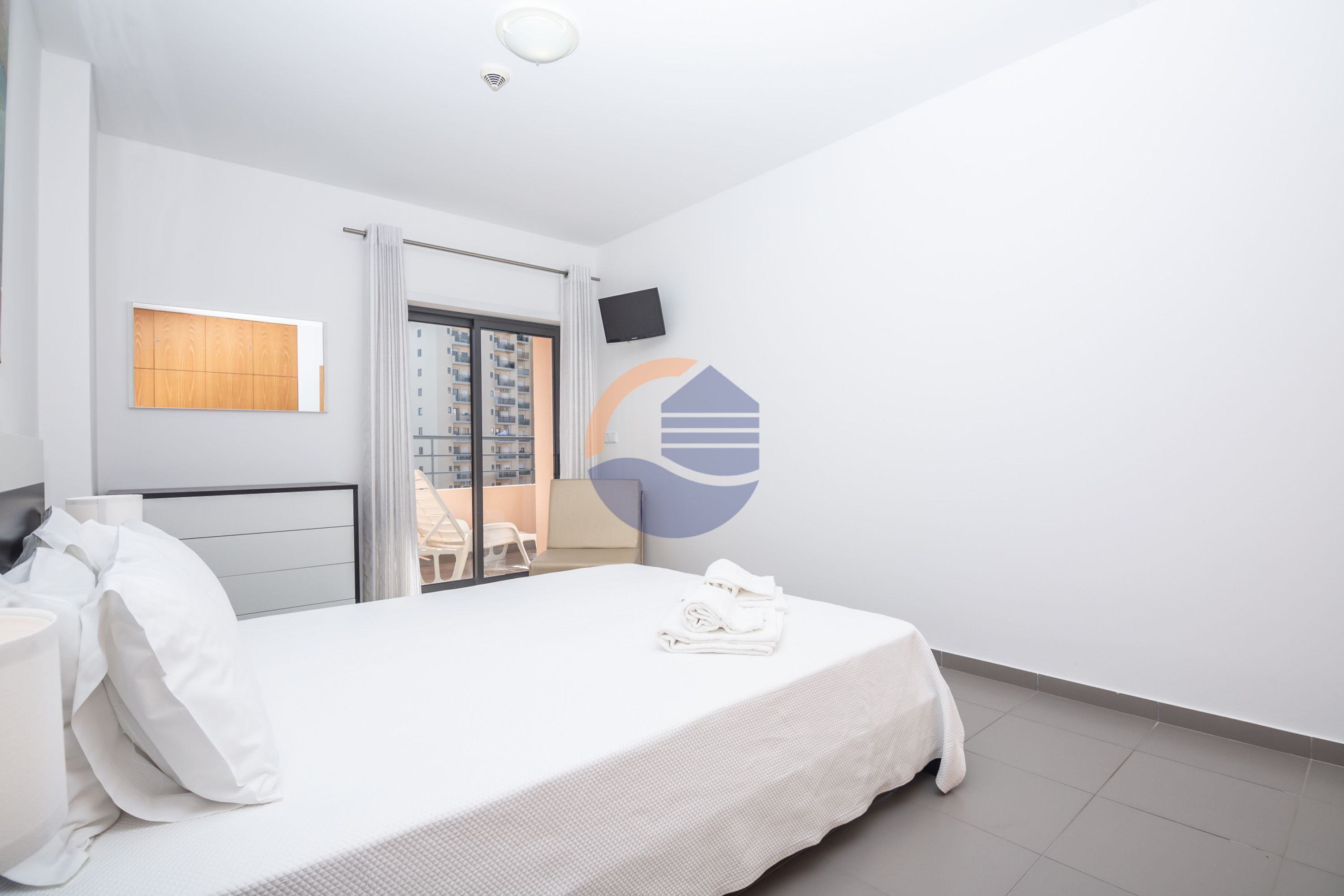 Ein Hotelzimmer mit einem Bett, einem Fernseher, einem Fenster mit Blick auf ein Gebäude und einer Tür, die auf einen Balkon führt.