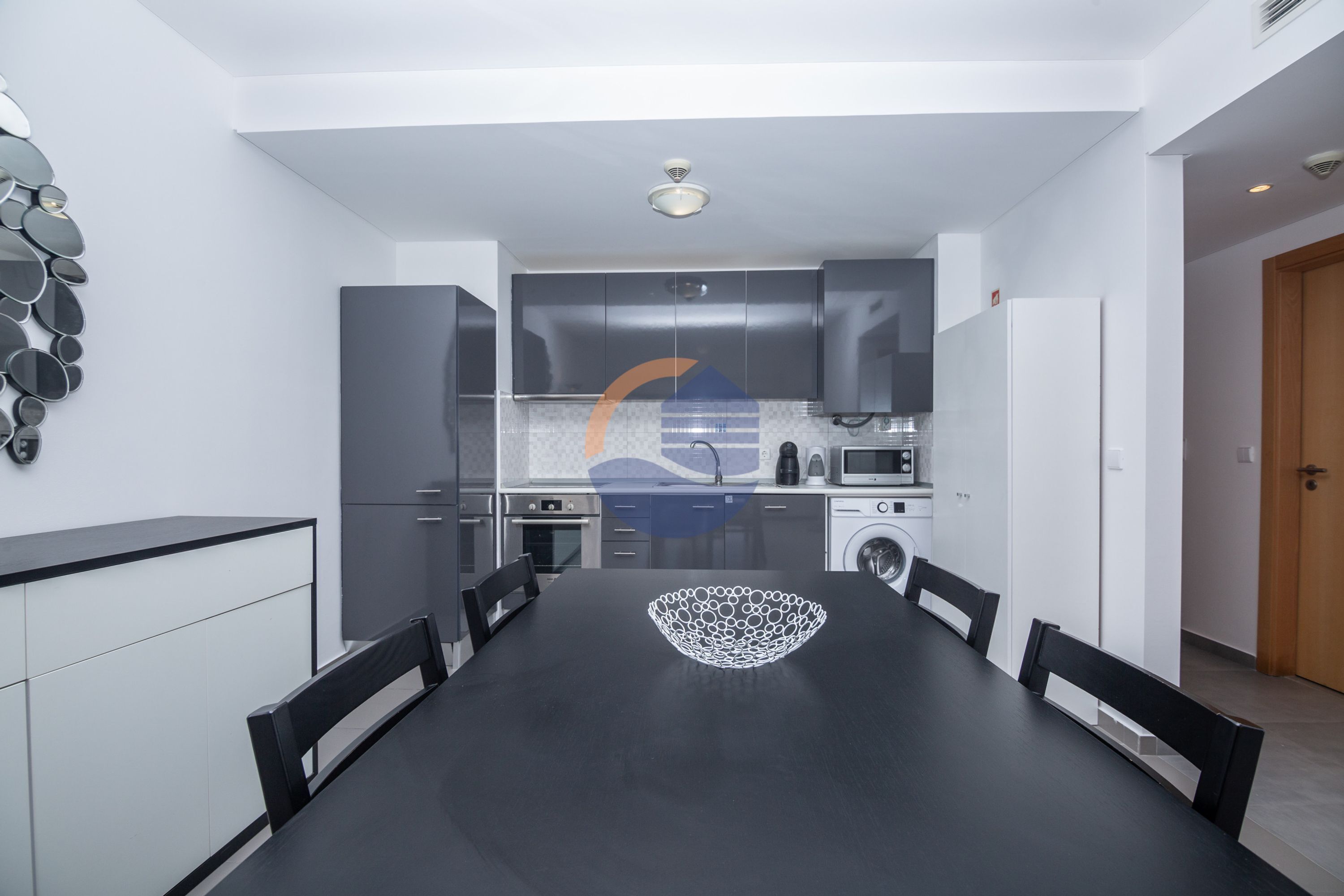A modern kitchen with grey cabinets, a built-in oven, microwave, and washing machine.
