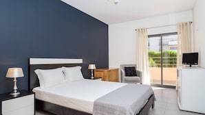 Habitación de hotel moderna con una cama grande, mesitas de noche, televisión, una silla y un balcón con vistas.