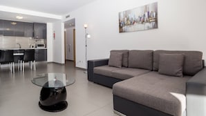 Una sala moderna con una mesa de centro de vidrio, sofá gris y un cuadro de un paisaje urbano en la pared.