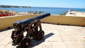 A cannon on a stone platform overlooking a beach with buildings and a clear sky. - 43 (Portimão)
