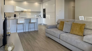 A modern kitchen with white cabinets, a central island with bar stools, and a grey sofa with mustard pillows. - 43 (Portimão)