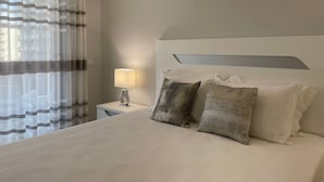 A hotel room with a bed, a nightstand, a lamp, and a window with sheer curtains. - 43 (Portimão)