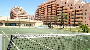 Una cancha de tenis con una red al frente, rodeada de edificios residenciales de varios pisos.