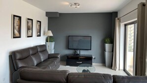 Una sala moderna con un sofá de cuero oscuro, una mesa de centro de vidrio, un televisor de pantalla plana y obras de arte enmarcadas en la pared.