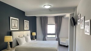 Un dormitorio moderno con una cama grande, dos mesitas de noche con lámparas, una silla y obras de arte en las paredes.