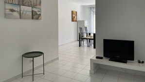 Ein modernes Wohnzimmer mit Flachbildfernseher, einem kleinen Beistelltisch und einem Essbereich mit Stühlen und Tisch.