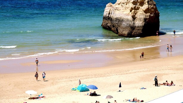 A beach with a large rock formation, clear blue water, and people enjoying the beach. - 27 - A420 in Portim o (Portimão)