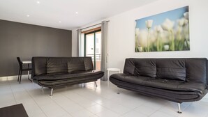 A modern living room with two black leather sofas, a dining table, and chairs. There is a large window with curtains, and a painting of flowers on the wall. - 27 - A420 in Portim o (Portimão)