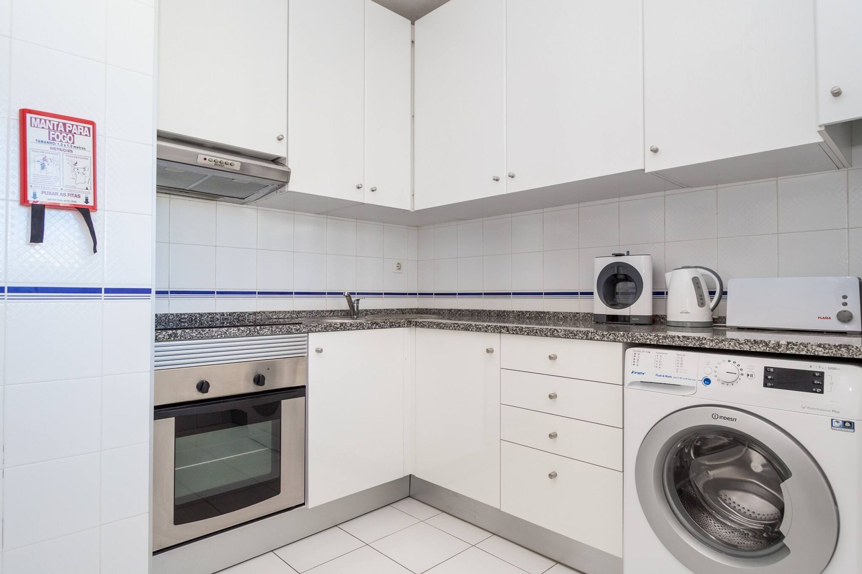 Une cuisine avec des meubles blancs, un four en acier inoxydable, un lave-linge et une machine à café.