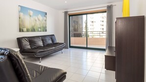 A modern living room with a black leather sofa, a painting of flowers, a sliding glass door to a balcony, and a dark wooden cabinet. - 27 - A420 in Portim o (Portimão)