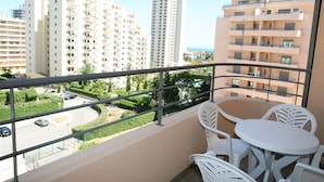 Un balcon doté de mobilier d’extérieur blanc, donnant sur un quartier résidentiel composé de plusieurs immeubles d’appartements.