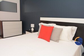 Una habitación de hotel moderna con una cama grande, una mesita de noche, una lámpara y un aparador.