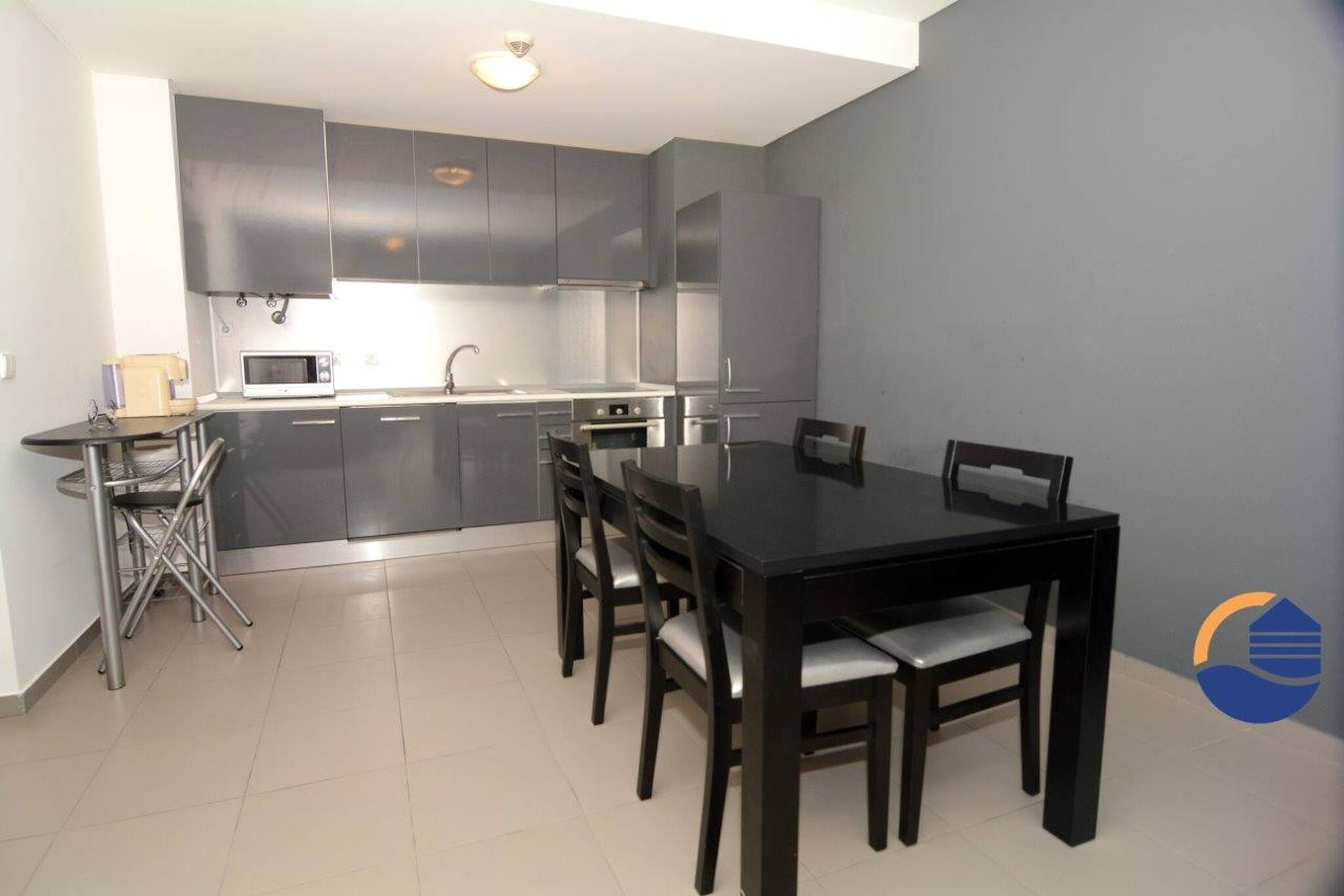 A modern kitchen with grey cabinets, a microwave, and a dining area with a black table and chairs.