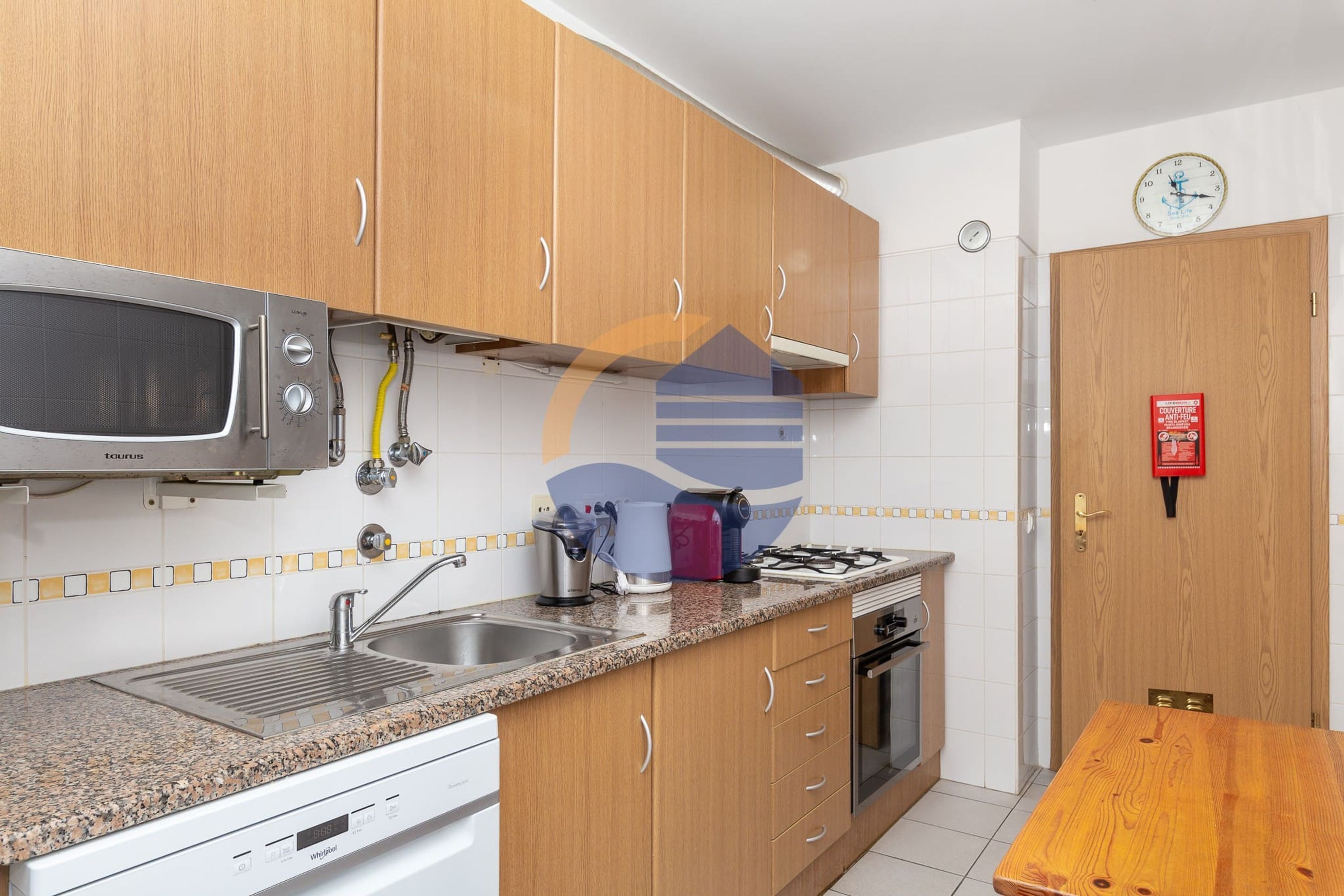 A kitchen with wooden cabinets, a microwave, a sink, a stove, and a clock on the wall.