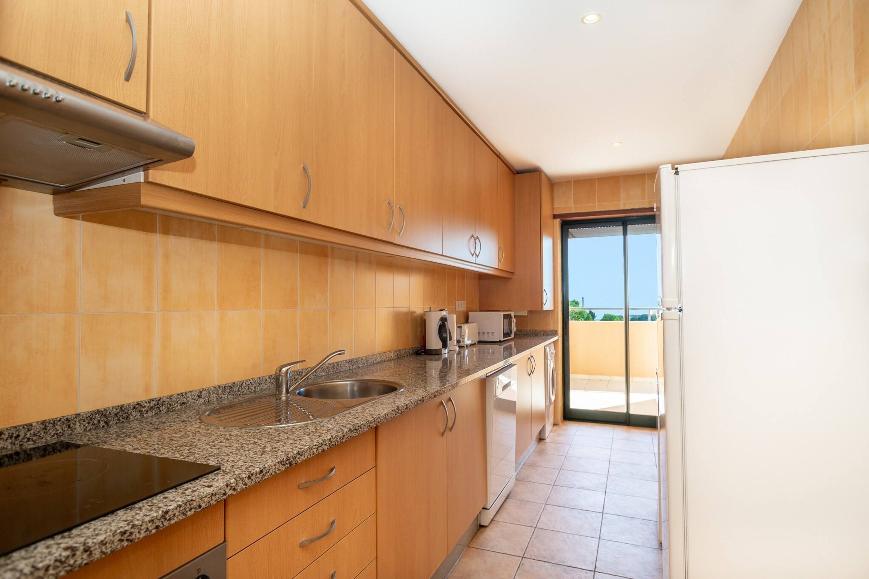 A modern kitchen with wooden cabinets, a granite countertop, stainless steel sink, and a built-in oven.