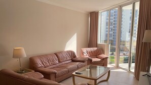 A modern living room with a sofa, armchair, and coffee table, large windows with curtains, and a view of high-rise buildings. - 41 (Portimão)