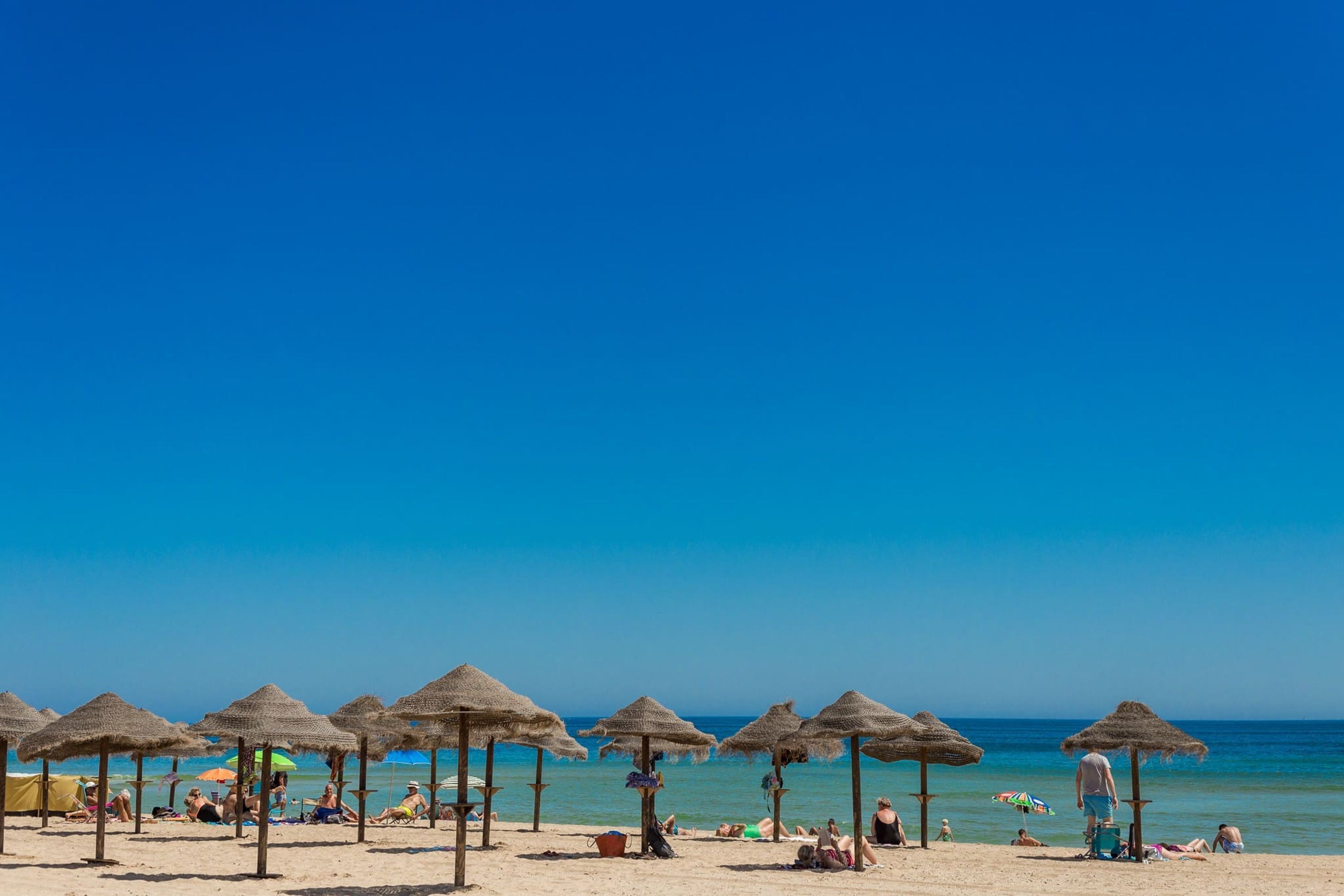 Ein Strand mit Reetsonnenstühlen und entspannten Menschen.