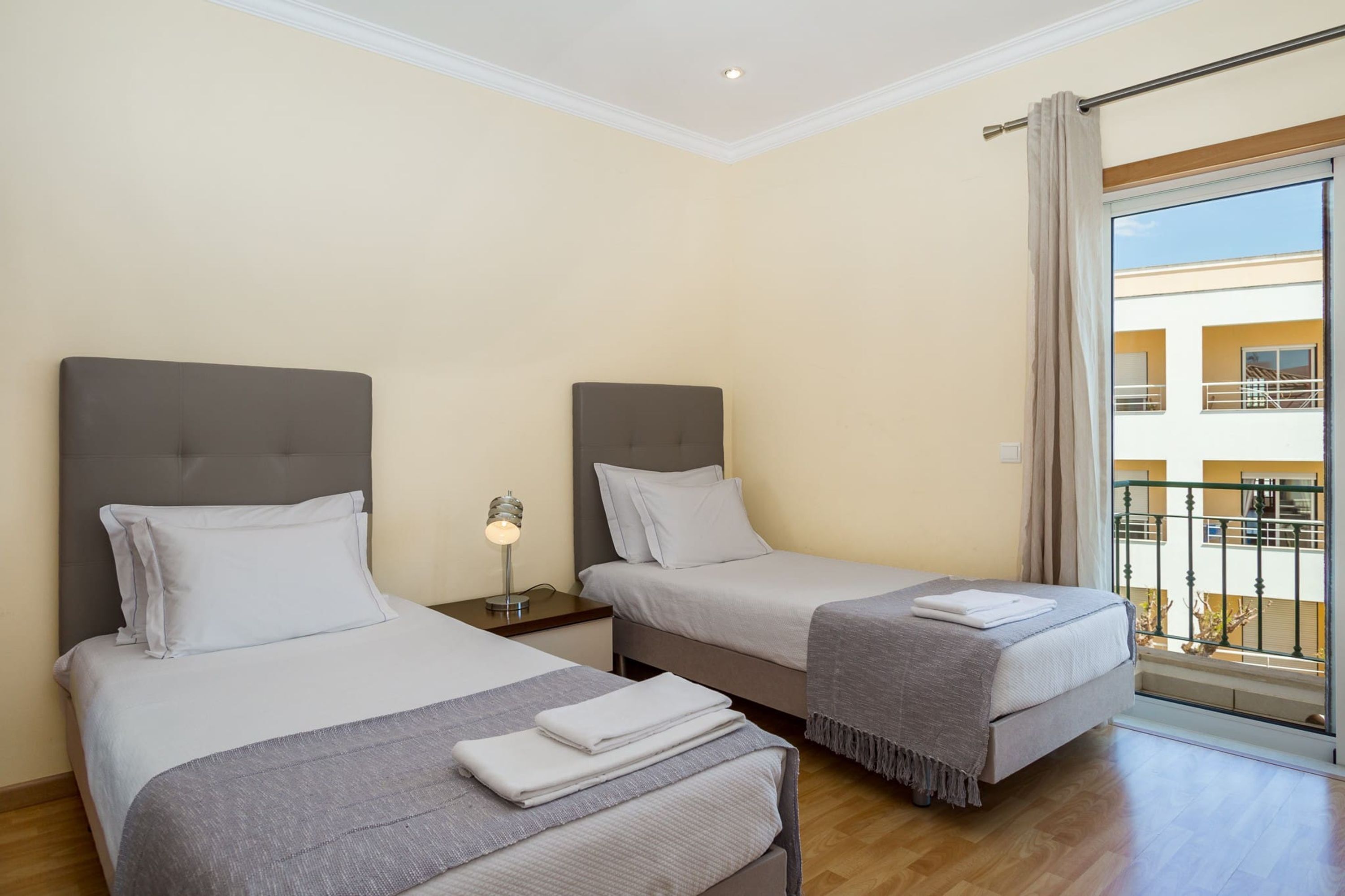 Ein Hotelzimmer mit zwei Betten, einem Nachttisch mit Lampe und einem Balkon mit Geländer.